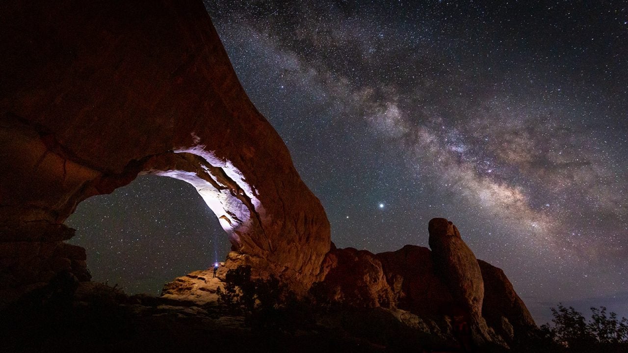 The Milky Way stretches across the dark night sky in Arches National Park.