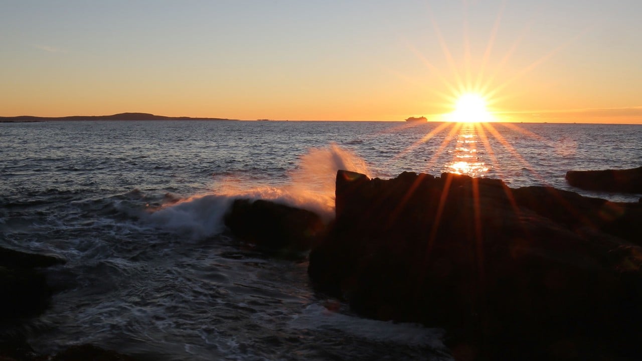 The sun rises as waves crash into the coastline.