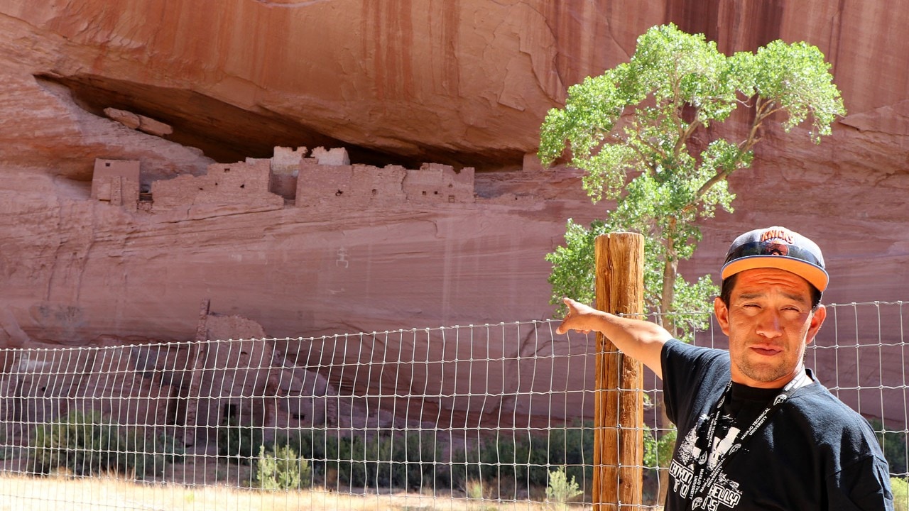 Navajo guide Harris Hardy points to a rock drawing below the buildings