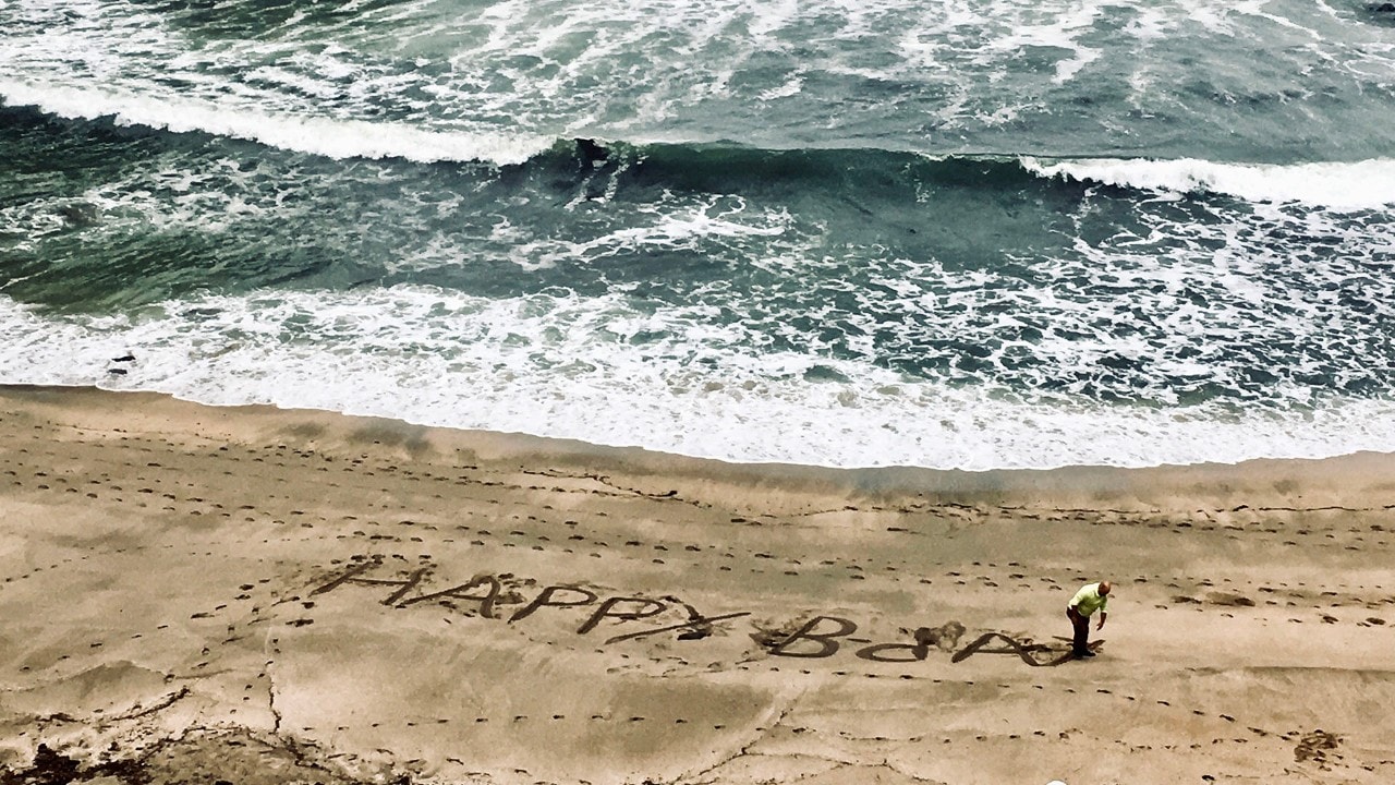 A man writes a birthday greeting in the sand at Shore Acres State Park.