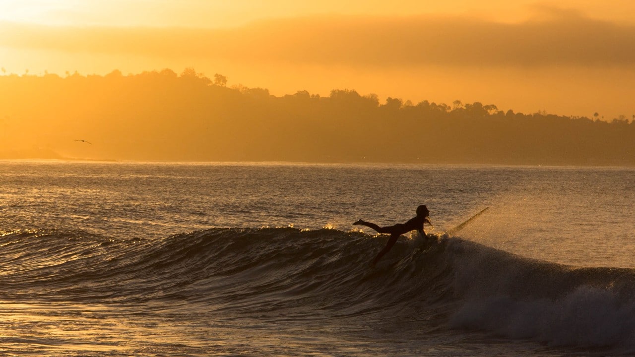 A surfer paddles out on Topanga Beach during sunset.