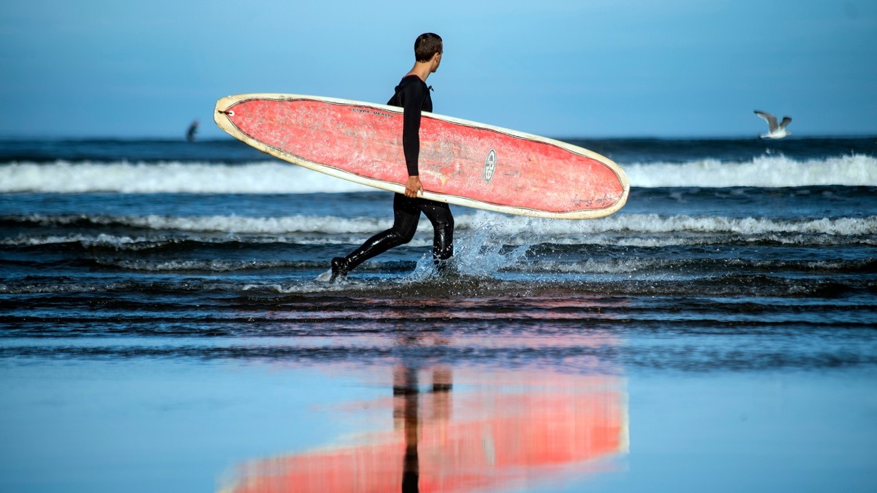 A surfer walks toward the surf break known as "The Cove" near Seaside, Oregon.