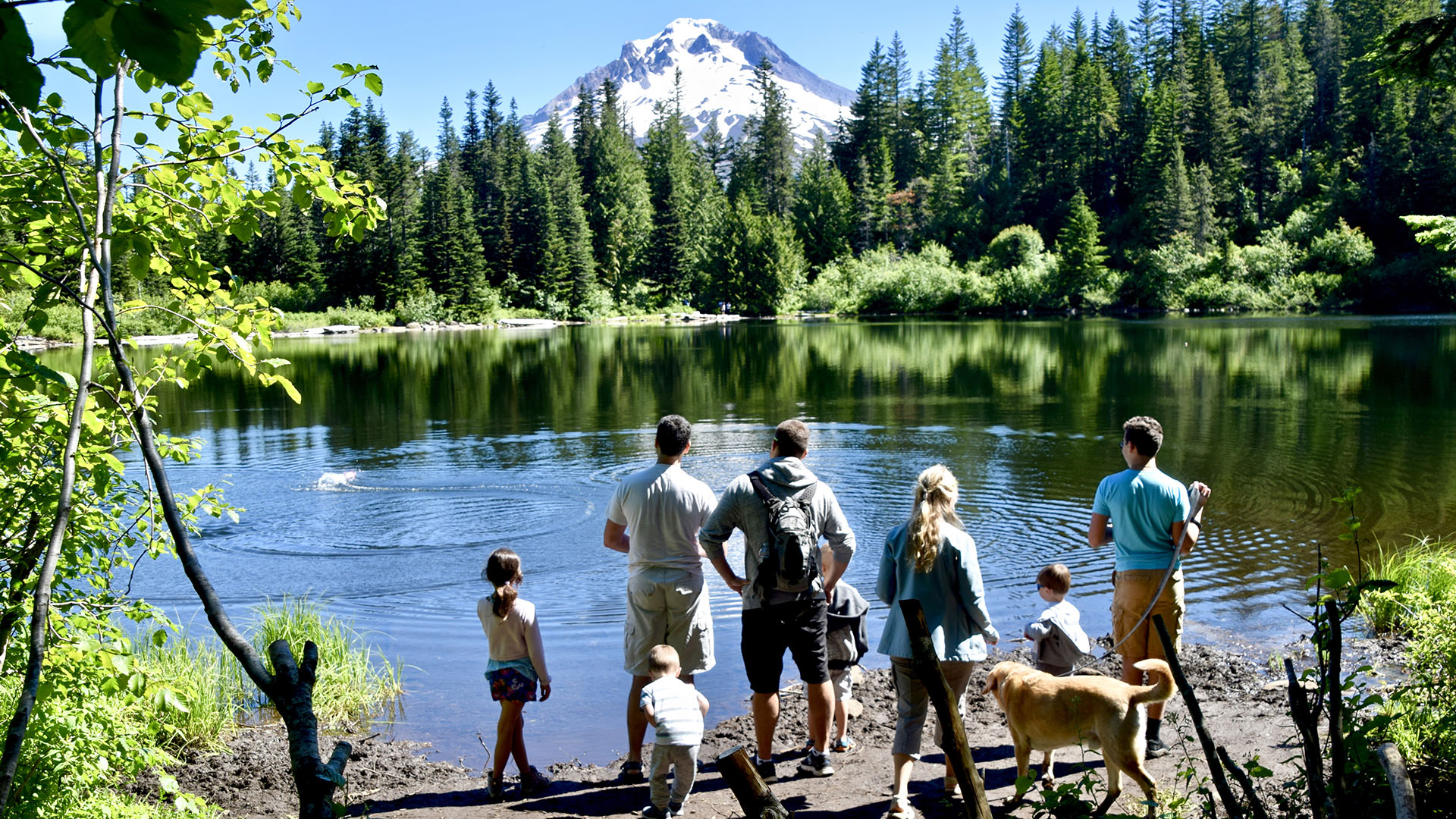 A family skips rocks in Mirror Lake, disrupting the reflection of Mt. Hood.