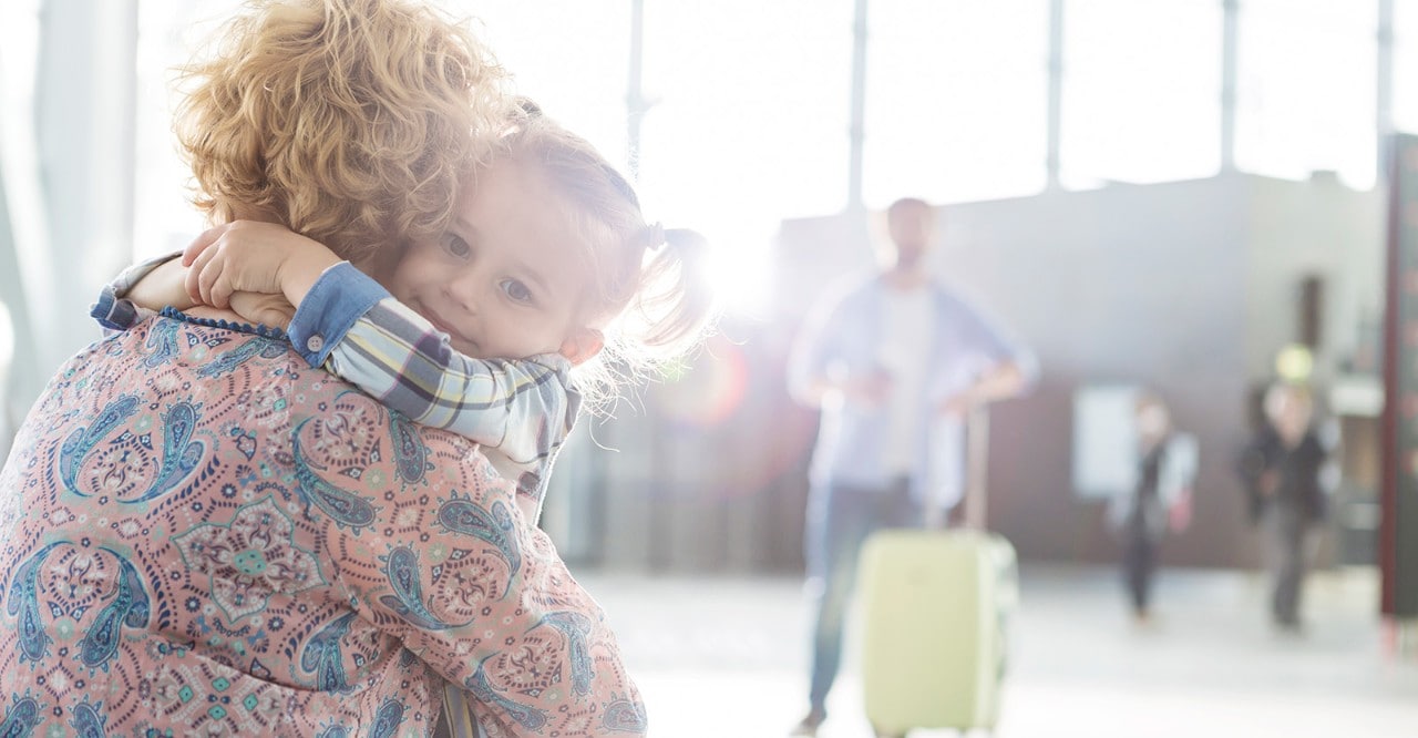 Mother and daughter hugging at the airport with father in background