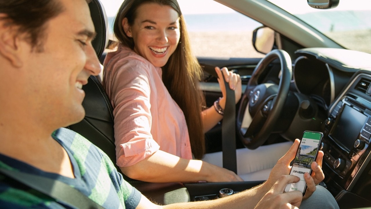 Woman driver smiling at male passenger who is looking at his phone