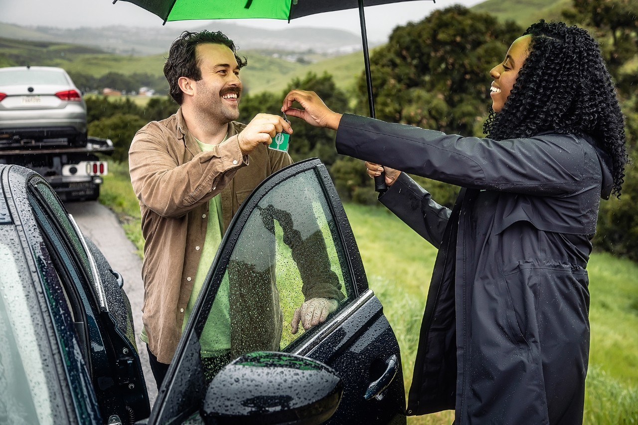 Woman handing man his rental car keys in front of the car in the rain.