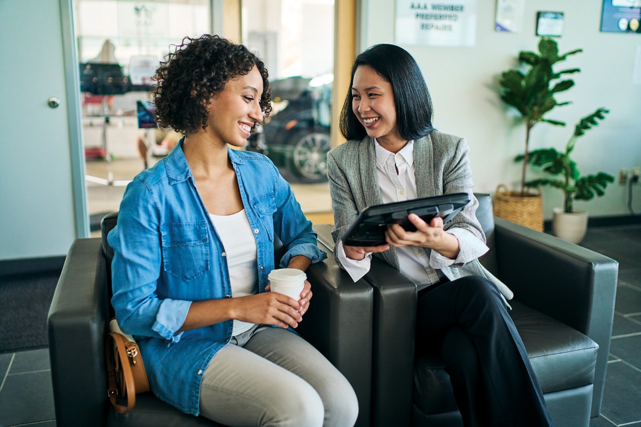 Two women sitting next to each other on chairs looking a tablet.