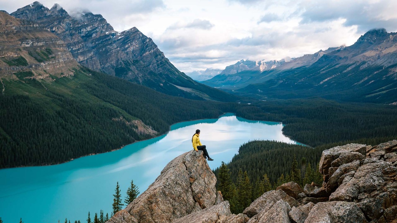 Person sitting at the peak of a rock formation with water in the background.