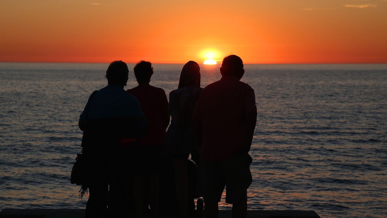 People watch the sun set over the Gulf of Mexico.