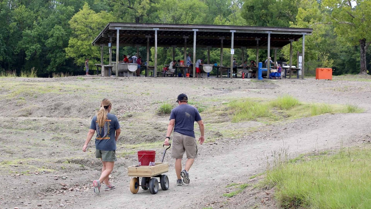 A couple pulls a bucket of dirt to a wet processing pavillion.