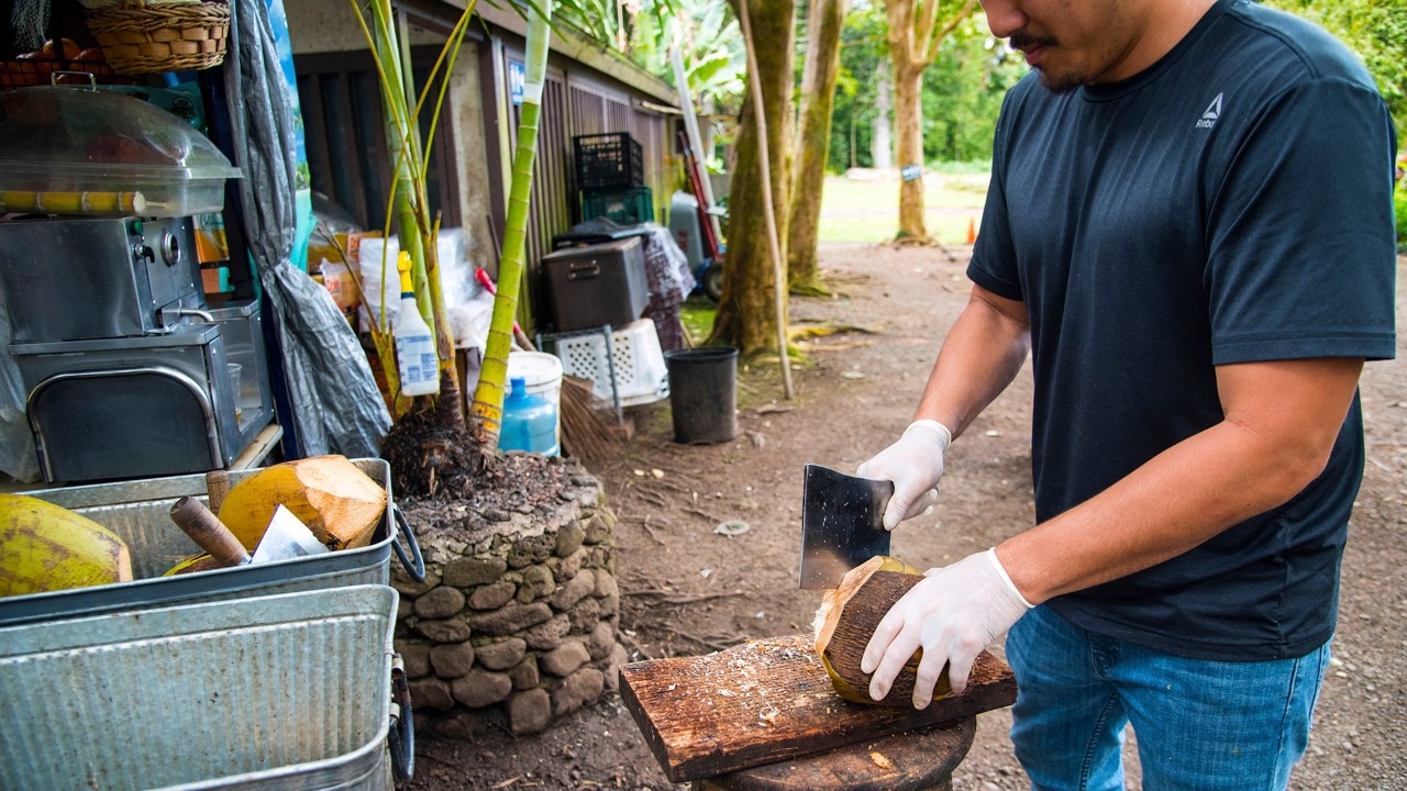 A vendor cuts open a fresh coconut. 