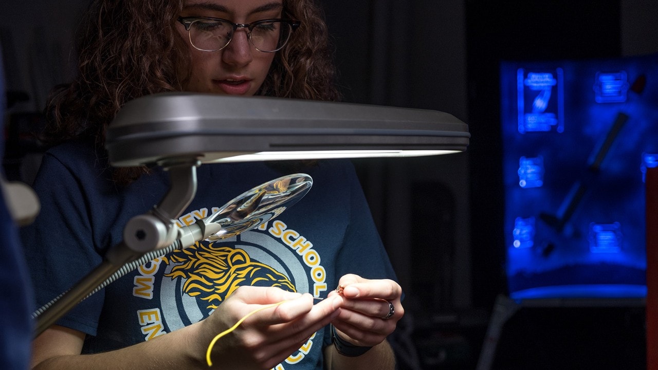 Alex, a junior in high school, threads wiring for the motor in her model rocket. 