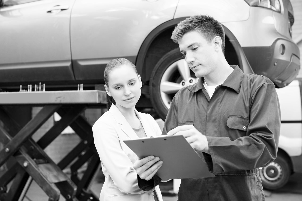 Car mechanic explaining car repairing expenses to a female customer. Horizontal shot.